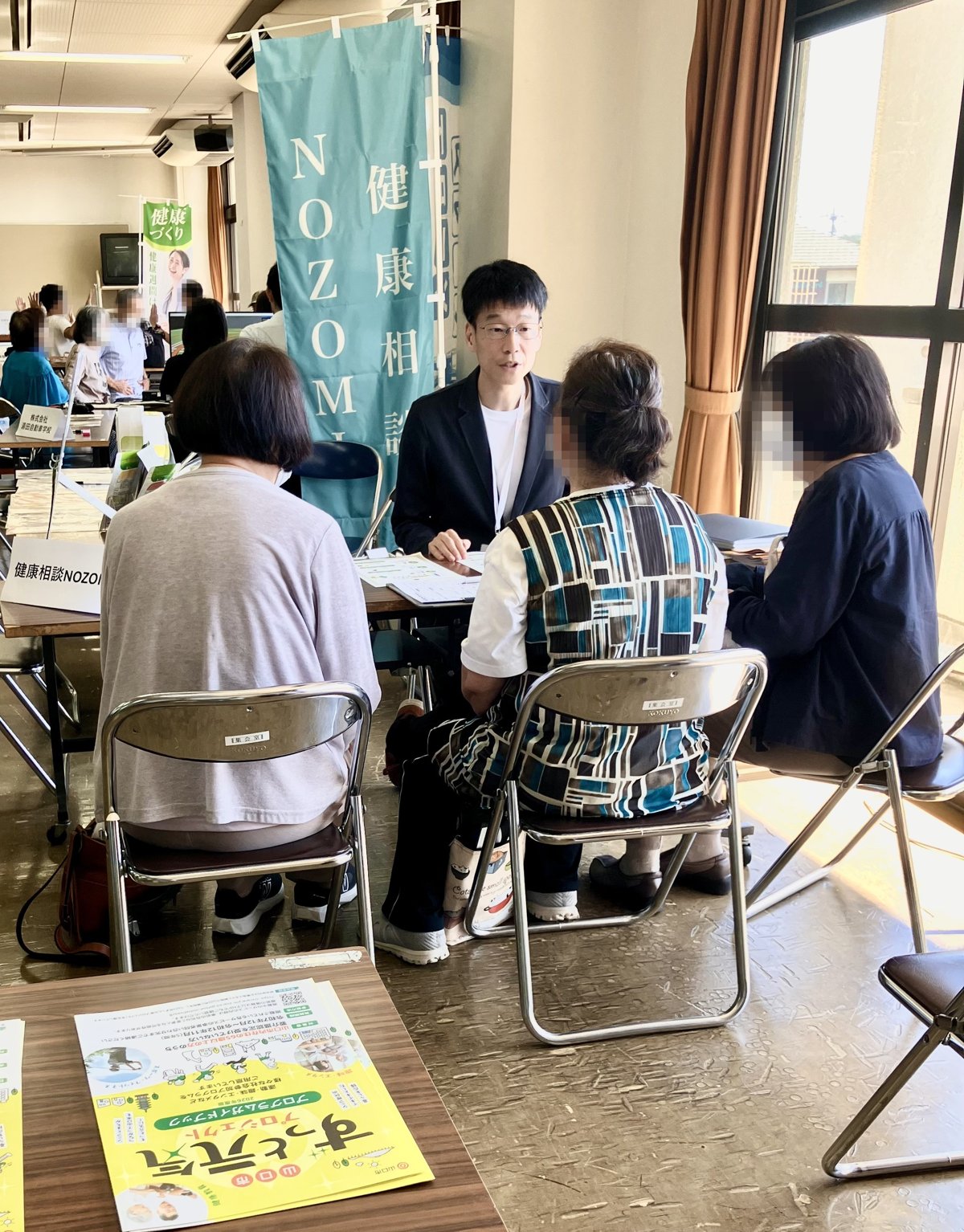 健康相談NOZOMIのブースで、テーブルを囲んで来場者の方とお話しする山本
